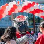 NC State students engage with Mr. Wuf beneath a decorative arch made of red and white balloons on Day of Giving.