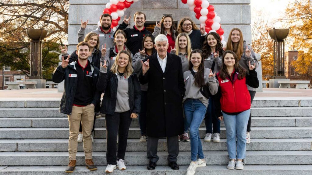 NC State Student Alumni Association members pose for a picture in front of a balloon-decorated Memorial Belltower.