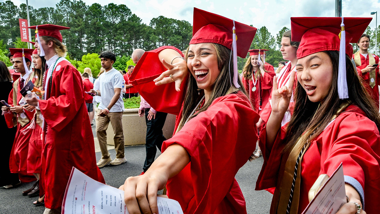 Two NC&#160;State graduates celebrate commencement in their Wolfpack Red caps and gowns.