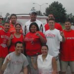 NC State Native American Alumni Network members, clad in the red and white of State, throw up the Wolfie hand sign for a group photo.
