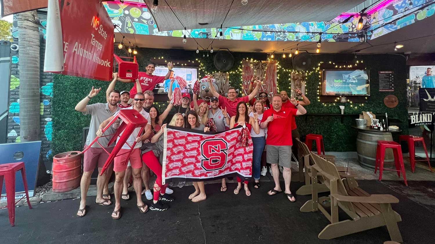 NC State Tampa Bay Alumni Network members pose with a Wolfpack flag as they catch the game at a local joint.
