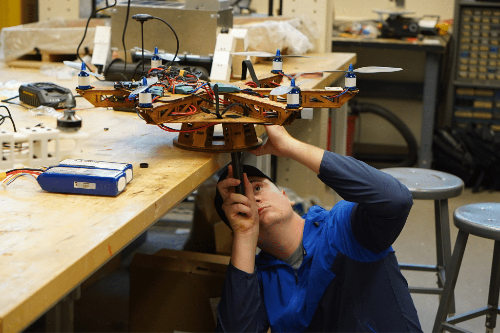 Student under an aircraft project, looking up while using a tool